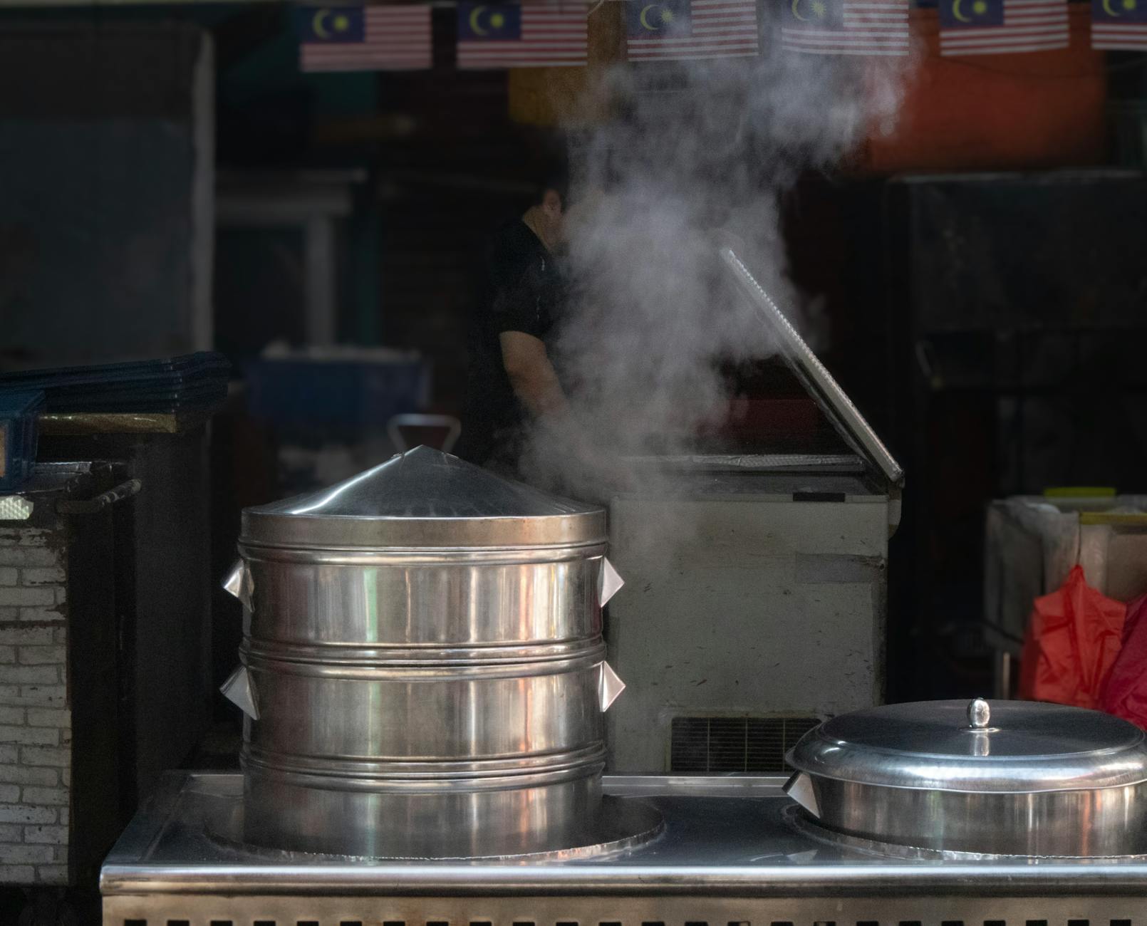 Steaming pot at a Malaysian street food stall with flags overhead.